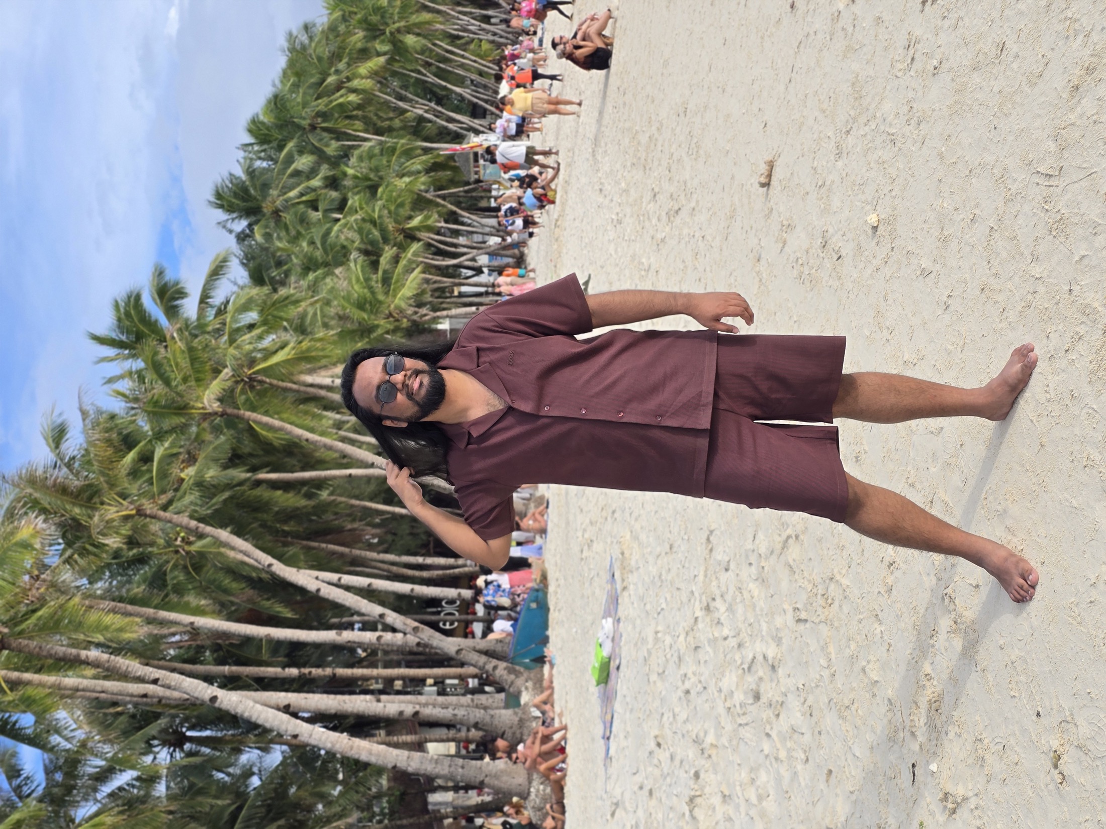 Suniv Ashraf on a palm-lined beach beneath a wide blue sky.