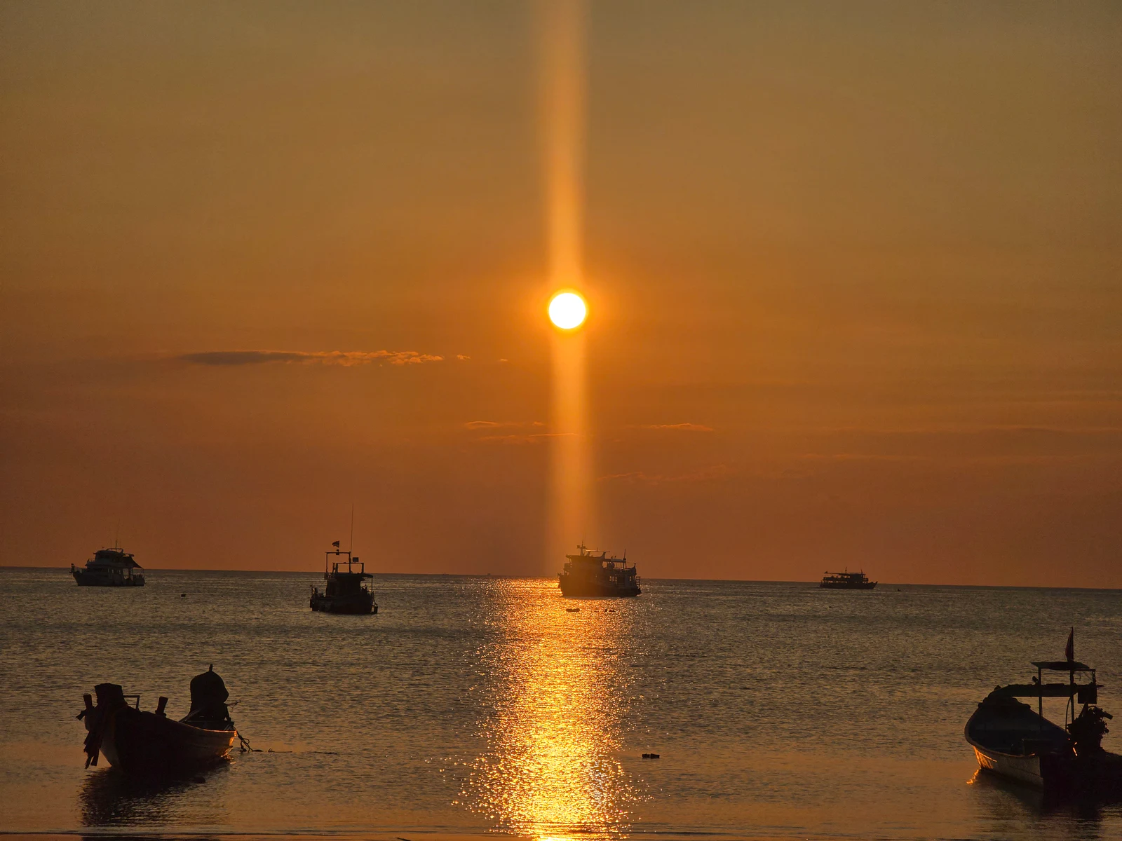Boats and a vertical sun reflection on a horizon.