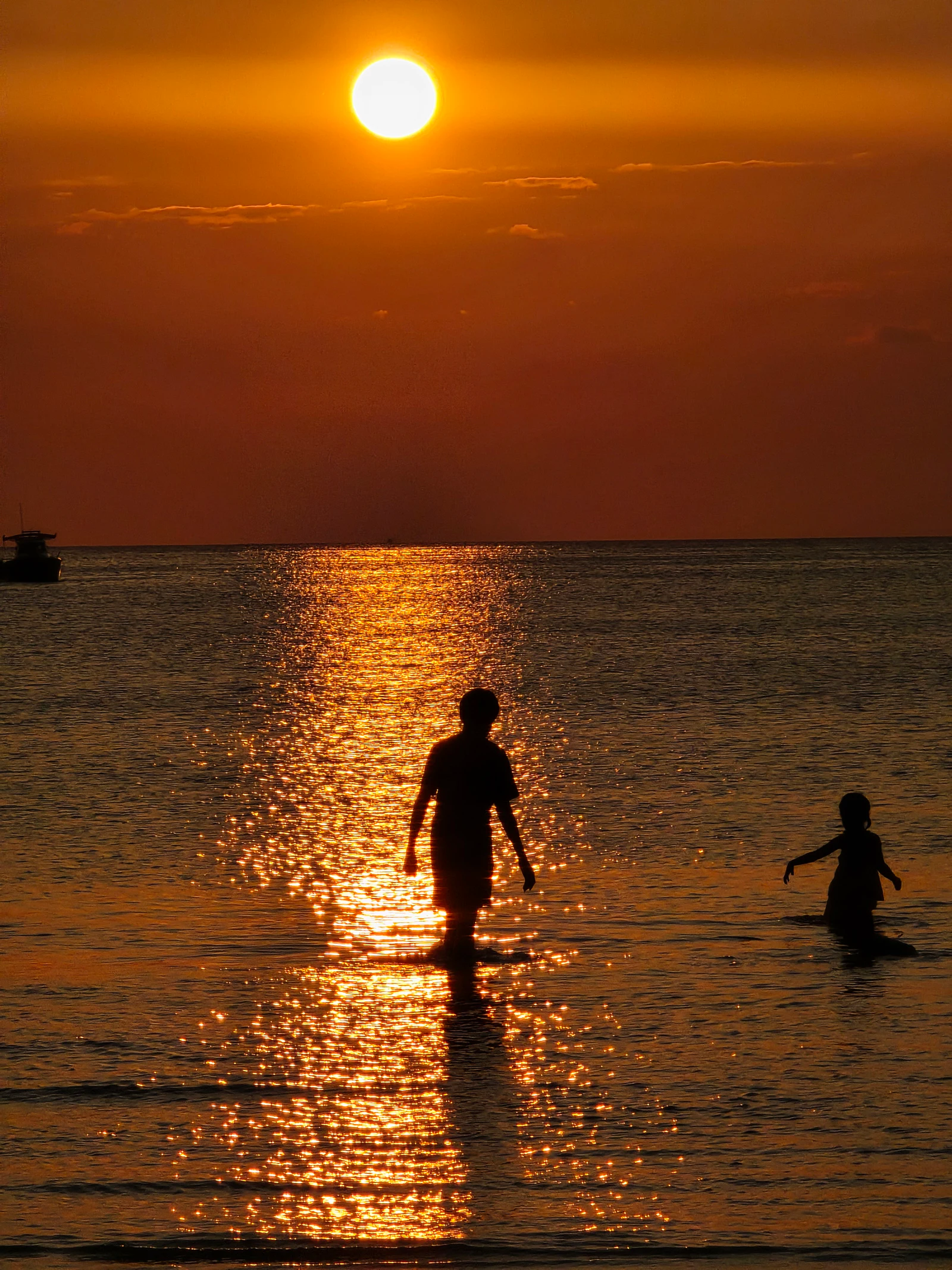 Silhouetted figures at sunset with a reflected path of light.